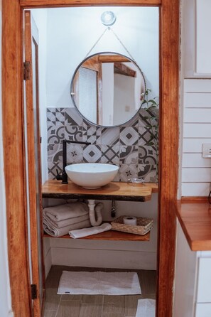 Une salle de bain avec un meuble-lavabo en bois, un lavabo blanc, un miroir rond et des carreaux décoratifs sur le mur.