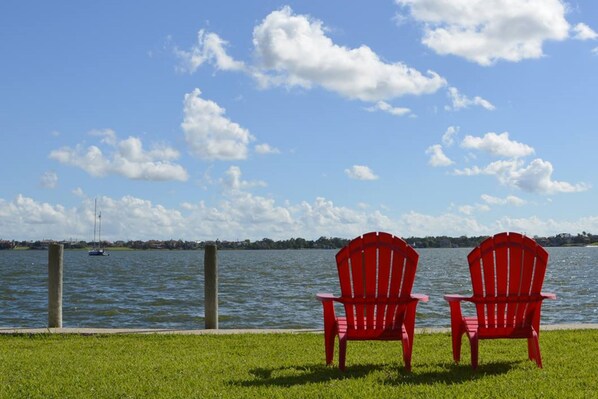 Deux chaises rouges sont placées face à une étendue d’eau, sous un ciel dégagé.
