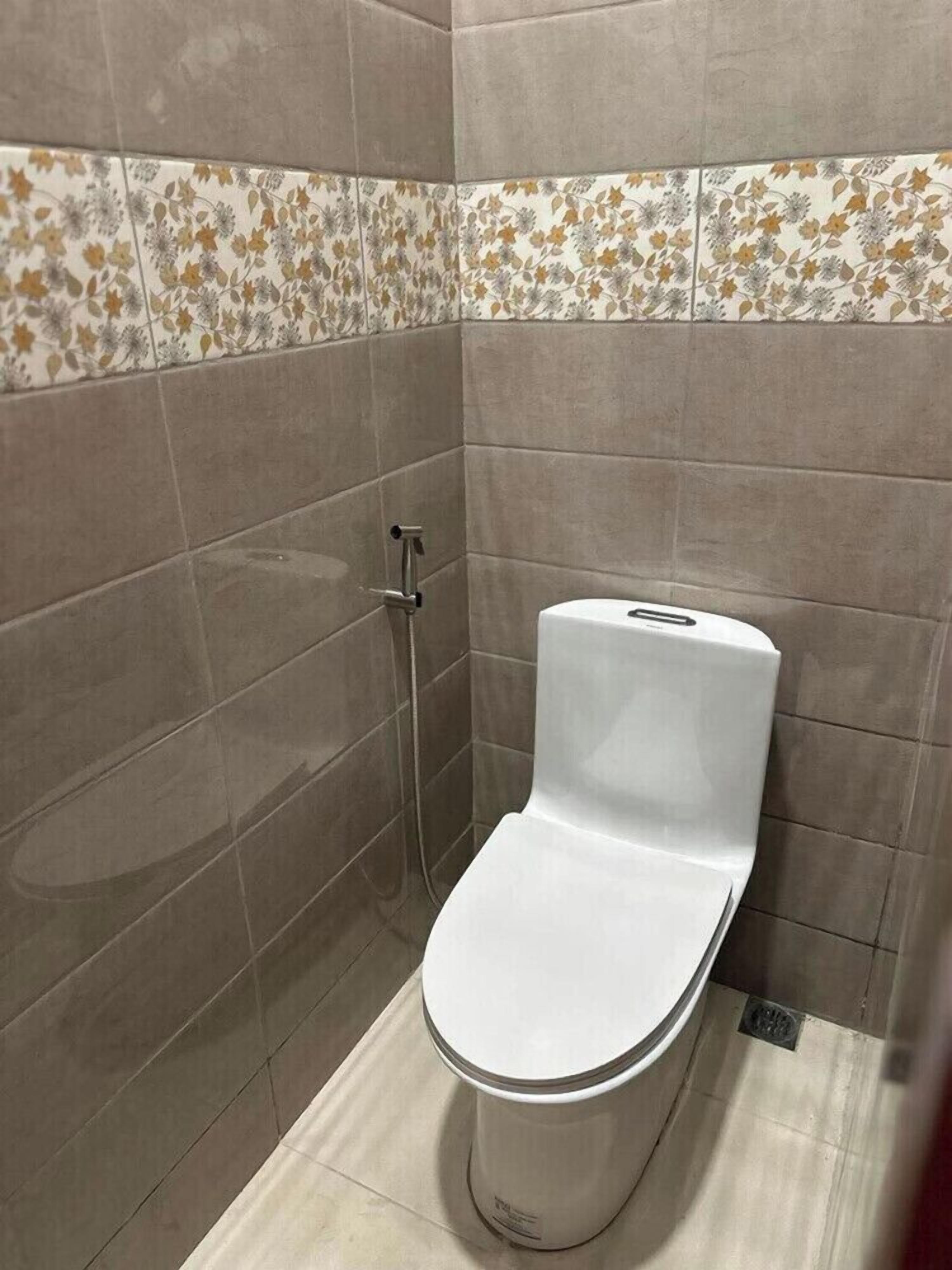 Un baño con inodoro, ducha y pared de azulejos con estampado floral.