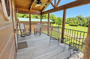 A wooden deck with a view of a green landscape, a rocking chair, and a table.