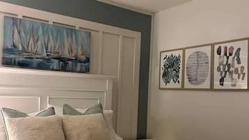 Un dormitorio con cama, ventilador de techo, pintura de veleros y arte abstracto en la pared.