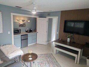 Un espacio habitable funcional con kitchenette, comedor, sofá, mesa de centro y televisor montado en la pared.