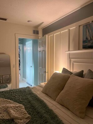 Un dormitorio con una cama, un ventanal grande y una puerta que da a otra habitación.