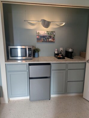 Una cocina compacta con microondas, cafetera y un refrigerador pequeño.