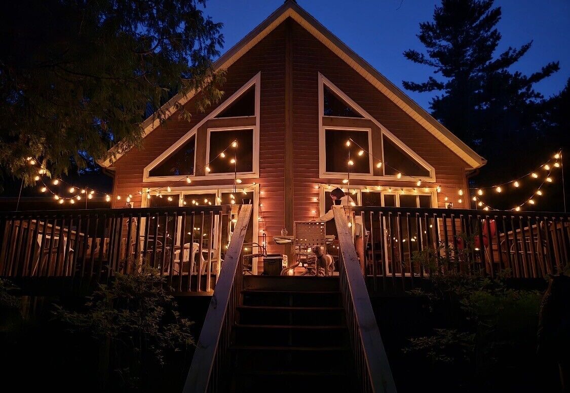 A wooden cabin with a staircase leading to a deck, surrounded by string lights.