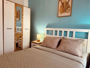 Een slaapkamer met een bed, nachtkastje, lamp en een kledingkast.