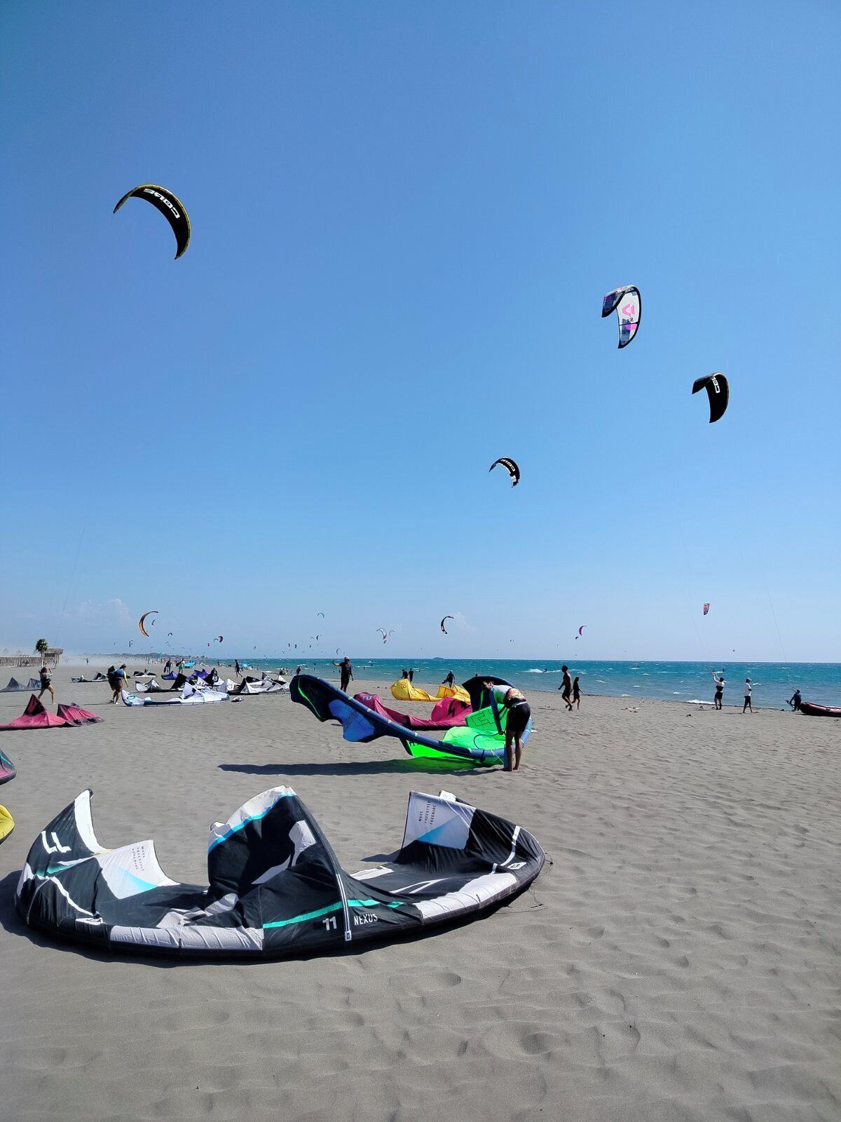 A beach with multiple kites and a large inflatable raft on the sand.