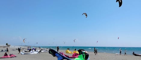 A beach with multiple kites and a large inflatable raft on the sand.