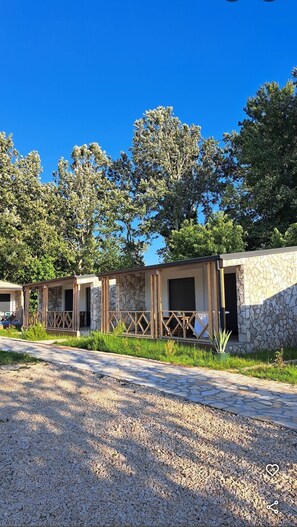 Una hilera de cabañas con paredes de piedra y vigas de madera, rodeadas de árboles y un camino de grava.