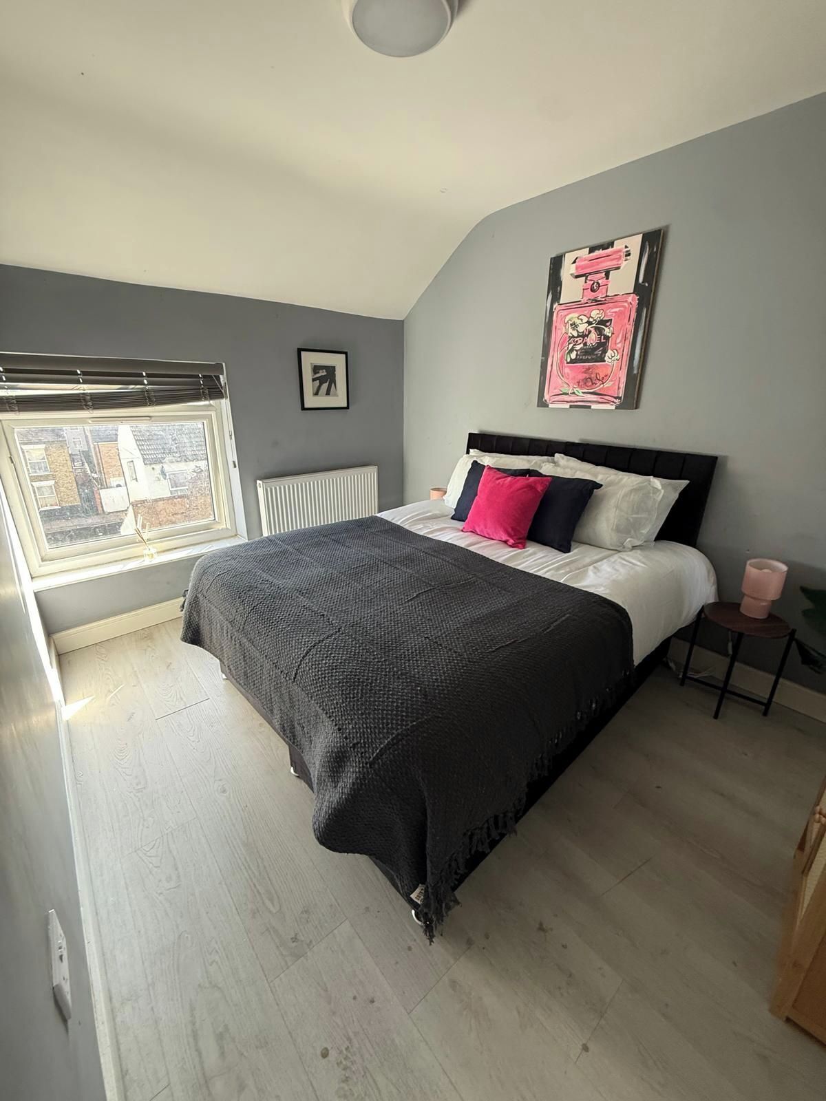 Une chambre à coucher avec un lit, un radiateur, une fenêtre et un tableau accroché au mur.