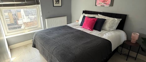 A bedroom with a bed, a radiator, a window, and a picture on the wall.
