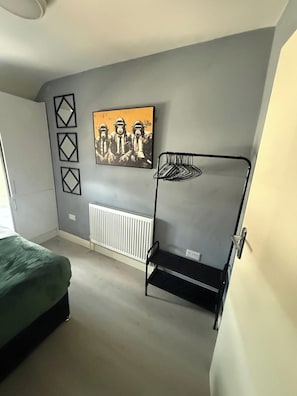 A bedroom with a bed, a radiator, a wall-mounted shelf, and a framed picture. - 2 Bedroom | Bedford | Stylish (Bedford)