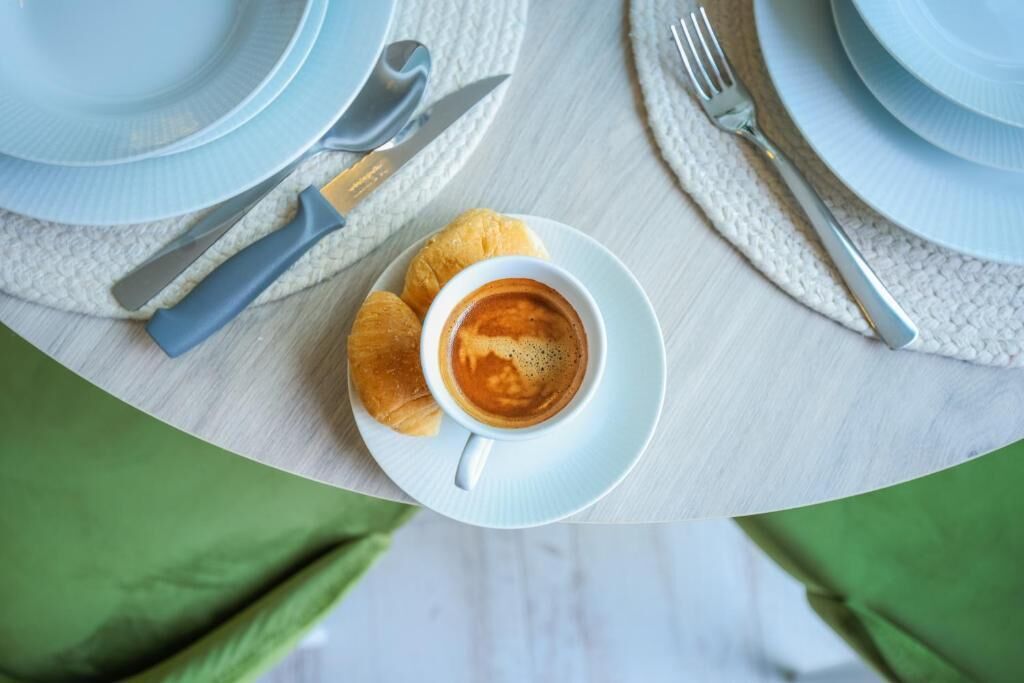 Una tavola apparecchiata con una tazza di caffè, croissant e posate.
