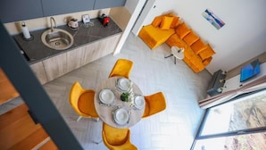 Una cocina moderna con un lavamanos, una zona de comedor con una mesa redonda y sillas amarillas, y un sofá naranja brillante en una sala de estar.