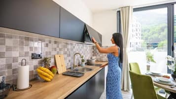Una cocina moderna con gabinetes oscuros, encimera de madera y vista a un edificio a través de un amplio ventanal.