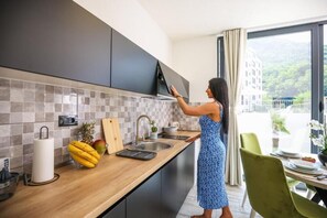 A modern kitchen with dark cabinets, a wooden countertop, and a view of a building through a large window.
