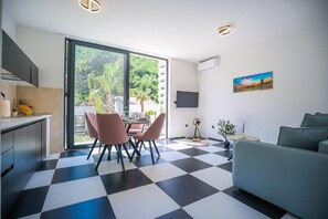 A modern living space with a checkered floor, a dining area with chairs, a sofa, a TV mounted on the wall, and a painting. - Rajska Dolina (Boreti)
