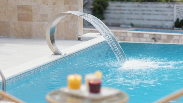 Una piscina amb una font d'aigua moderna i una taula amb espelmes.