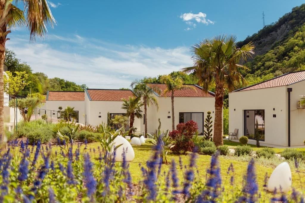 Ein modernes Hotel mit mehreren Zimmern, einem gepflegten Garten mit verschiedenen Pflanzen und einer Bergkulisse.