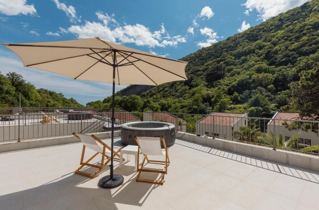 Una terraza en la azotea con un paraguas grande, dos sillones de descanso y un jacuzzi.