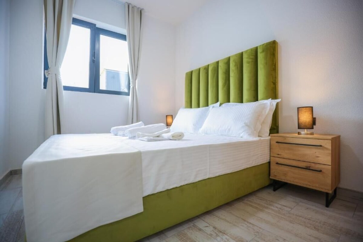 A hotel room with a large bed, a bedside table with a lamp, and a window with curtains.