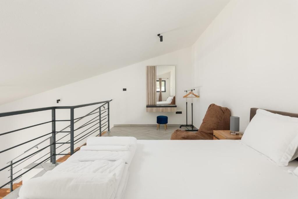 Un dormitorio con cama, mesita de noche, lámpara colgante, espejo y una escalera.