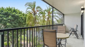 Ein Balkon mit Tisch und Stühlen mit Blick auf einen Garten mit Palmen.
