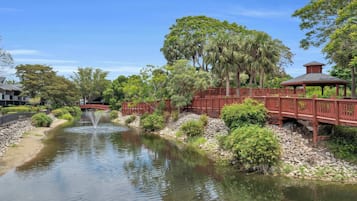 A tranquil waterway with a wooden bridge and gazebo, surrounded by lush greenery and trees.