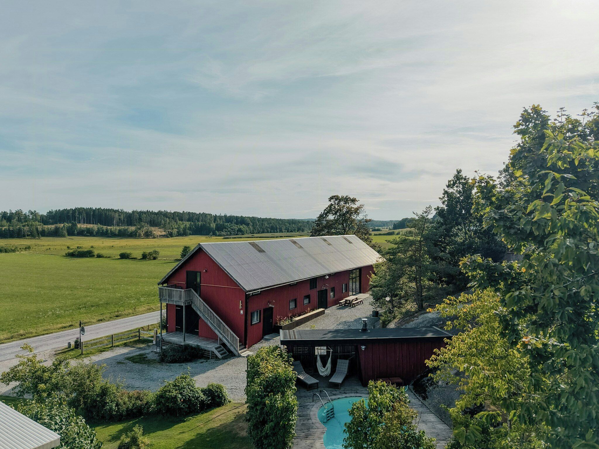 A red barn with a staircase, a swimming pool, and a paved driveway.