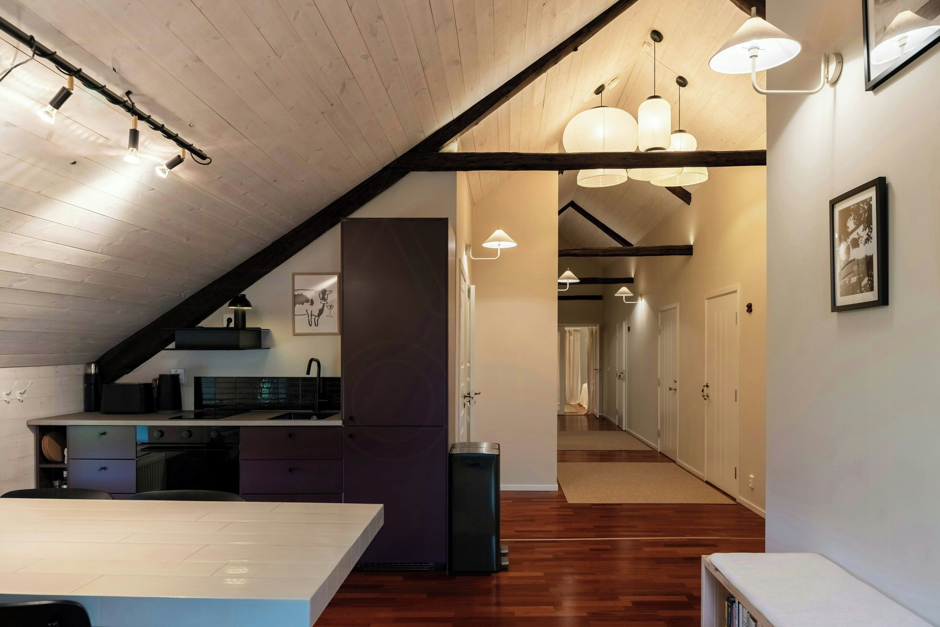 Une cuisine moderne avec un plafond en bois, des luminaires suspendus et une vue sur un couloir avec des portes.