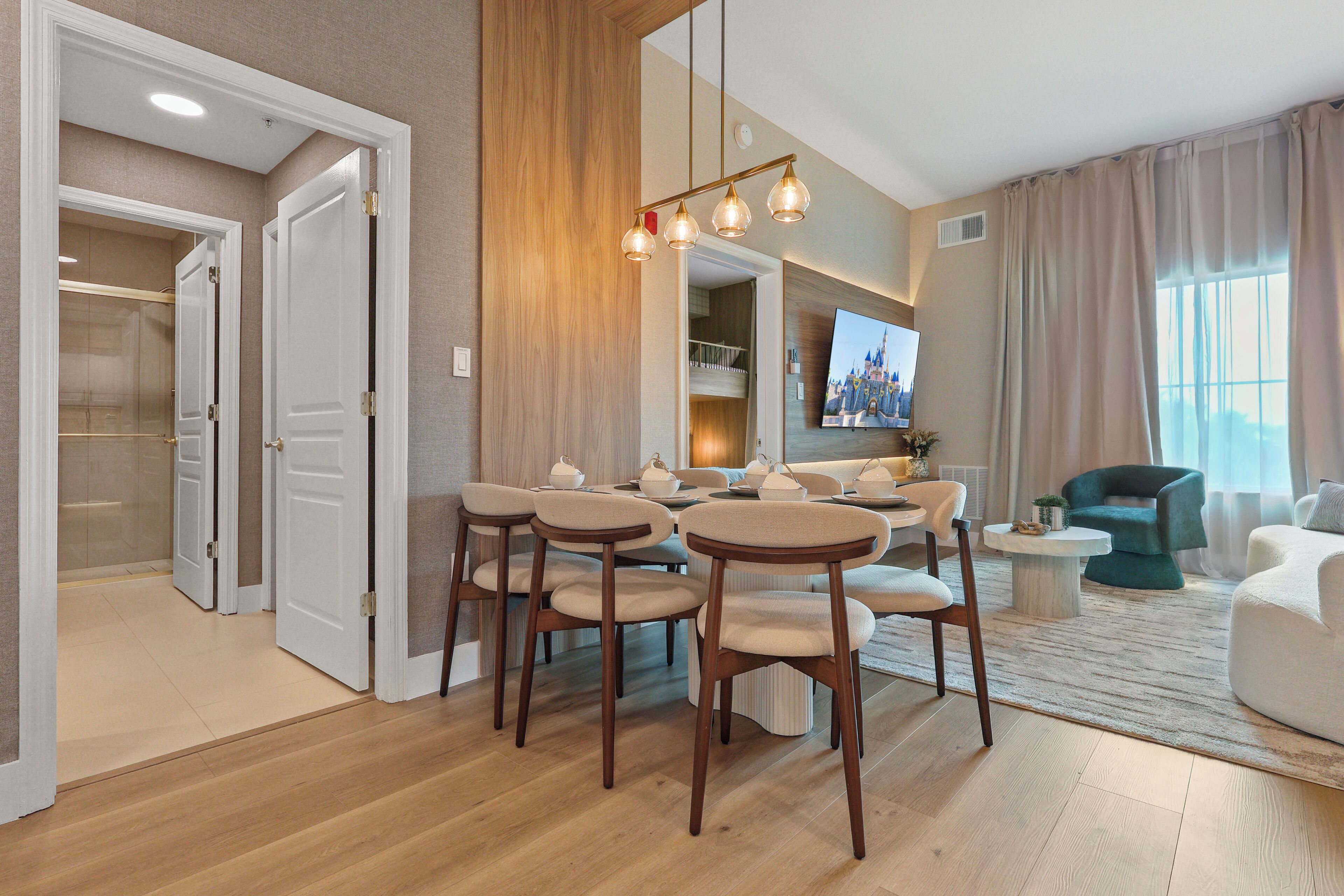 A modern living room with a dining area, wooden flooring, and a large flat-screen TV mounted on the wall.