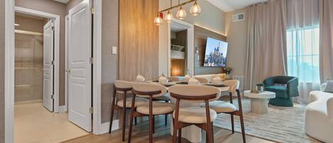 A modern living room with a dining area, wooden flooring, and a large flat-screen TV mounted on the wall.