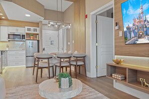 A modern kitchen with built-in appliances, a dining area with a round table and chairs, and a wall-mounted TV displaying a castle. - 2BR apartment with 4 queens and 2 twins (Orlando)