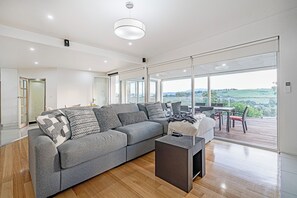 Ein modernes Wohnzimmer mit einem grauen Ecksofa, einem Couchtisch und einem Essbereich mit Blick auf die Landschaft.