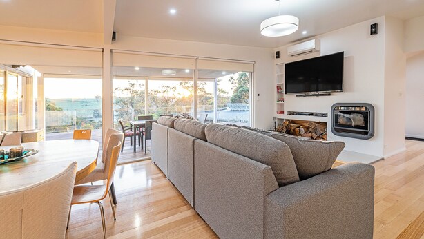 Uma sala de estar moderna com um amplo sofá modular, uma área de jantar com mesa redonda e uma TV na parede.