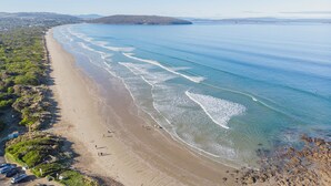 Uma praia costeira com águas cristalinas, areal arenoso e paisagem acidentada ao fundo.