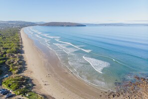 A coastal beach with clear waters, a sandy shore, and a hilly landscape in the background. - Golden Hours Serene Bushland Outlook and Outdoor Spa (Forcett)