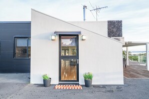 Een modern gebouw met een zwarte deur, twee potplanten en een welkomstmat.
