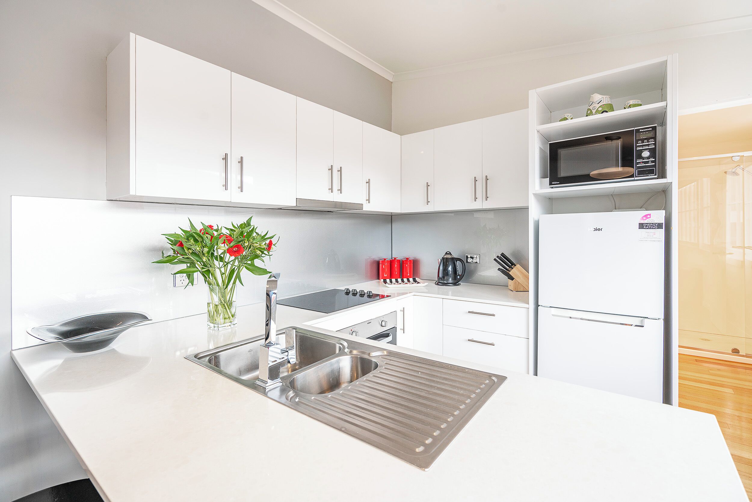 A modern kitchen with white cabinets, a stainless steel sink, a microwave, and a refrigerator.