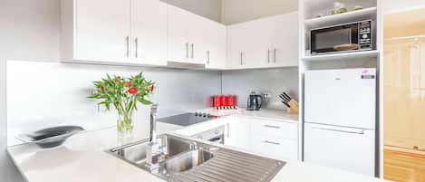 Une cuisine moderne avec des meubles blancs, un évier en acier inoxydable, un four à micro-ondes et un réfrigérateur.