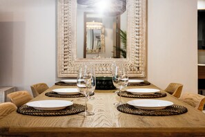 A dining table set with plates, cutlery, and wine glasses, surrounded by chairs. - NEW! Apartment at Laguna Beachside: 2 bedrooms (Tambon Choeng Thale)