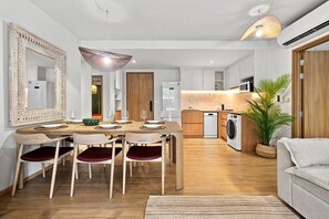 Une cuisine moderne avec des armoires blanches, un lave-vaisselle encastré et un coin repas comprenant une table et des chaises en bois.
