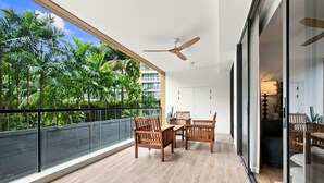 Un balcón con una mesa y sillas de madera, un ventilador de techo y vistas a palmeras.