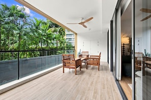 Een balkon met een houten tafel en stoelen, een plafondventilator en uitzicht op palmbomen.