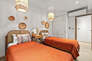 A modern bedroom with two beds, a wooden desk, and decorative wall hangings. - NEW! Apartment at Laguna Beachside: 2 bedrooms (Tambon Choeng Thale)