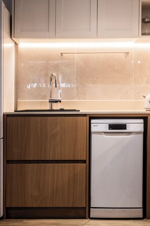 A modern kitchen with a built-in dishwasher, wooden cabinets, and a stainless steel faucet. - NEW! Apartment at Laguna Beachside: 2 bedrooms (Tambon Choeng Thale)