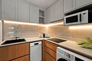A modern kitchen with white cabinetry, a built-in microwave, a dishwasher, and a sink. - NEW! Apartment at Laguna Beachside: 2 bedrooms (Tambon Choeng Thale)