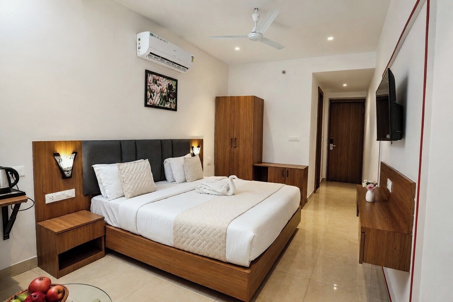 A modern hotel room with a bed, bedside tables, a TV, and an air conditioning unit.
