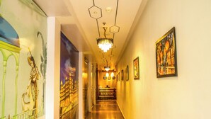 A hotel reception area with a long hallway, a reception desk, and a chandelier. - Hotel JHD Luxury Stay Restro & Sky Bar (Udaipur)