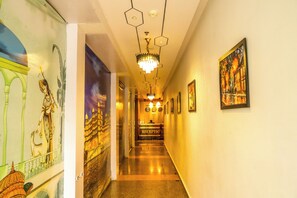A hotel reception area with a long hallway, a reception desk, and a chandelier. - Hotel JHD Luxury Stay Restro & Sky Bar (Udaipur)